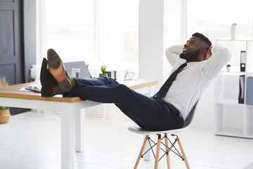 Joyful young manager relaxing on chair in white modern office