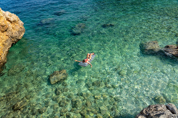 woman floating on an airbed over the cristal clear water of the rocky scenic mali bok orlec natural wild beach on cres island croatia