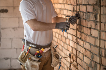 Electrician installer with a tool in his hands, working with cable on the construction site.