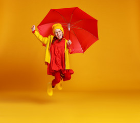 happy emotional cheerful child girl jumping and laughing  with red umbrella   on colored yellow background.