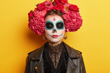 Traditional holiday in November. Female with sugar skull drawn with smile, wears flower wreath,...