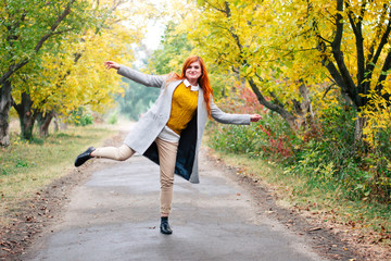 Portrait of a beautiful red-haired woman in autumn park fooling around and being silly