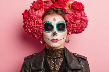 Close up portrait of beautiful woman with traditional mexican face painting, has eyes shut, wears...