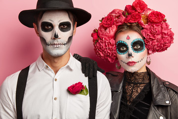 Serious woman and man have traditional mexican image, wear sugar skulls, dressed in special attire...