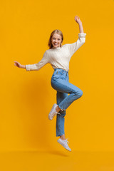 Fototapeta na wymiar Happy teen girl having fun, jumping on orange studio background