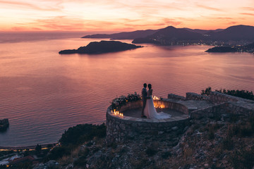 The bride and groom admire the beautiful sunset and natural landscape in Montenegro.