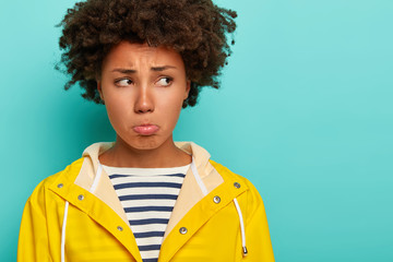 Gloomy pity woman with curly hairstyle, has frowning upset face expression, purses lips and looks...