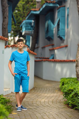 Young boy posing in summer park with palm trees. Cute spectacled smiling happy teen boy 11 years old, looking at camera. Kid's outdoor portrait.