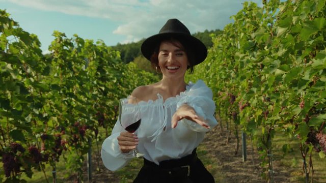 Gorgeous nice-looking young woman in happy mood running with wineglass on grape plantation enjoying life on vineyard vacation.