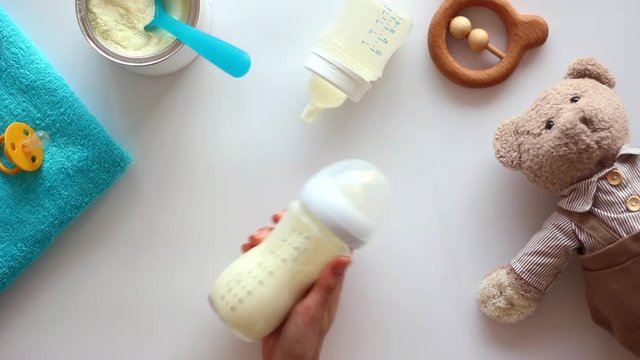 Hand holding the baby bottle with milk on white table with toys. Top view