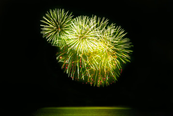 Beautiful fireworks display on evening black sky. In green and golden color holiday background with copy space for text