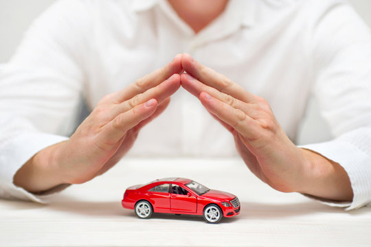 Car protection. Small red car covered by man hands. Car (automobile) insurance and collision damage waiver concepts