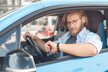 Young adult man sitting in car, looking on watch