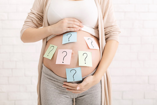Confused pregnant woman with question marks on paper stickers on tummy