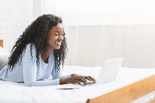 Cheerful young girl typing on laptop in bedroom