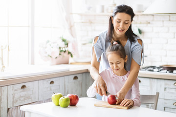 Mother teaching her little daughter how to make fruit salad