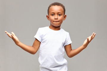 Children, lifestyle and body language. Isolated shot of cool handsome African American little boy having confident look biting lower lip and making gesture with palms, showing he is not afraid