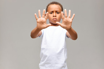 Portrait of serious Afro American little boy dressed in white t-shirt frowning having grumpy facial expression, showing all ten fingers on both hands at camera, making No gesture or Stop sign - Powered by Adobe