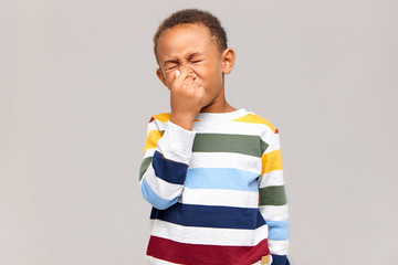 Ugh, disgusting! Portrait of emotional disgusted African American boy closing eyes and pinching...