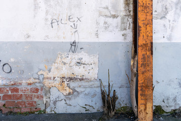 Abandoned factory wall with white and gray paint, exposed bricks and a rusty iron pillar