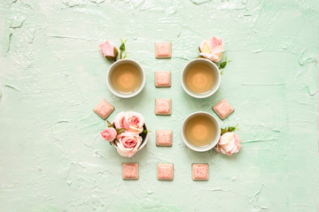 Set of cups with rose tea, rose buds blossom, pink chocolate pieces on trendy neo mint backdrop. Tea ceremony or tea advertisement, flat lay for restaurant, concept of relaxation and rest, meditation