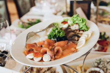 Close-up of cold fish such as salmon and tuna served on white oval ceramic dish with greenery, lemon and caviar. Wedding festive banquet.