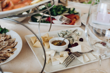 Close-up of square platter of assortment of fresh cheese served with honey and grapes at wedding table.