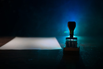 Close up view of rubber date stamper on wooden table with dark toned foggy background.
