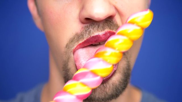 close-up, bearded man with painted lips eats a lollipop.