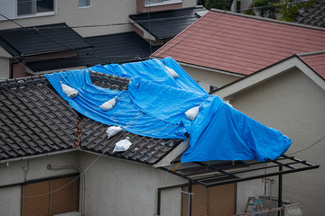 Tattered blue tarp on roof after strong typhoon wind damage - obrazy, fototapety, plakaty