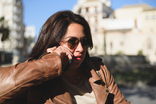 mujer con gafas de sol hablando por teléfono, sentada en la calle 