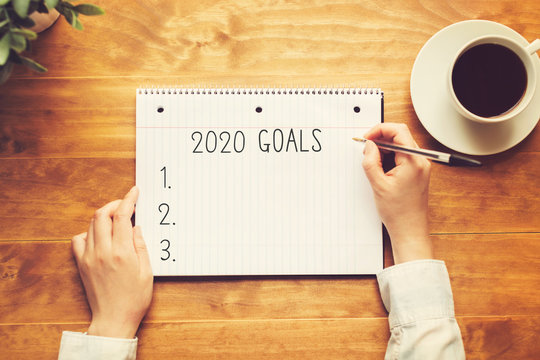 2020 goals with a person holding a pen on a wooden desk
