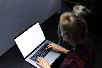 Young blonde girl typing on laptop with white mockup.