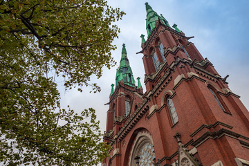 Helsinki.Finland. St. John Church in Helsinki. Bottom view of the Lutheran Church on the background of green trees. Religious building. Brick Church with a green roof. Cathedral spires against the sky