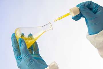 Hands in medical gloves holding a flask and pipette with a chemical liquid. The study of the properties of chemical liquid. Analysis of food products. The study of the composition of the detergent.