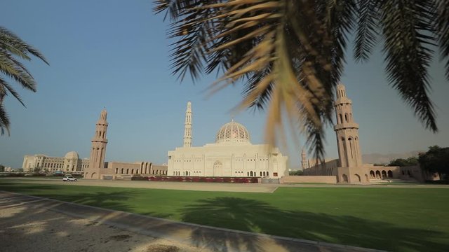 Muscat, Oman - February, 2019: Beautiful view of the Sultan Qaboos Grand Mosque. Amazing Islamic architecture. Camera movement between tall spreading palm trees. Panning motion