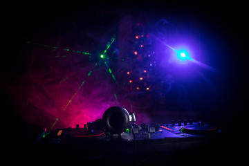Dj mixer with headphones on dark nightclub background with Christmas tree New Year Eve. Close up view of New Year elements on a Dj table. Holiday party concept. - obrazy, fototapety, plakaty