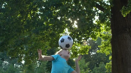 Male boy playing ball in yard kicking up with head, child sport club, activity