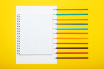 Notebook and color pencils on a yellow background. Mock up with copy space for your ideas. Flat lay style.