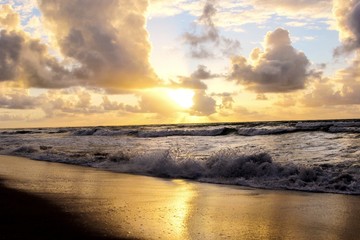 Obraz premium Waves and cloudy sky in the tropical sunset. Orange sky and golden reflection in the water. Guarajuba beach, Bahia, Brazil