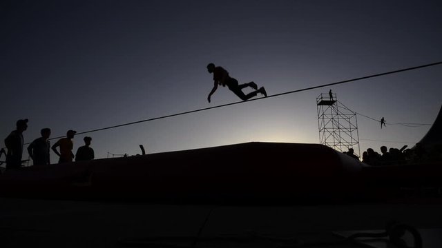 backlight Young man  balanced on slackline, on the beach, during sunset