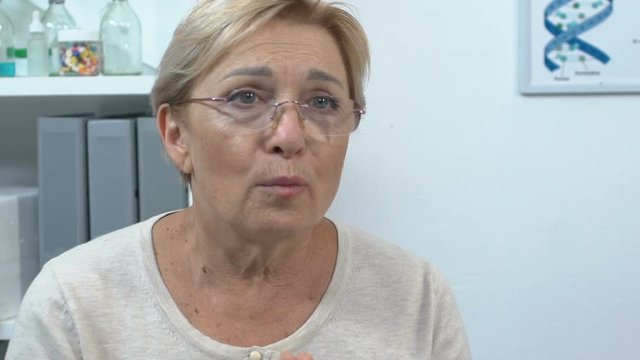 Upset senior woman talking to doctor in clinic, bad diagnosis news, slow motion