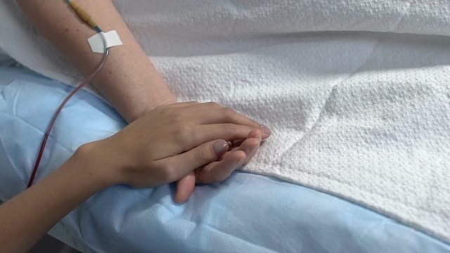 Relative holding ill woman by hand in hospital ward, support in sickness