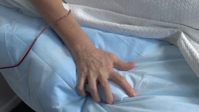 Hand of sick senior patient squeezing bed sheet in hospital, suffering pain