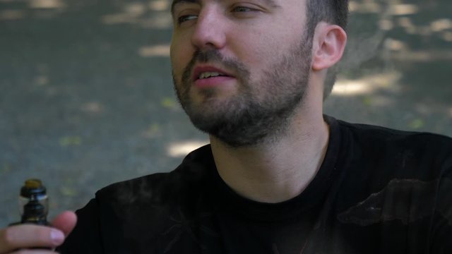 Handsome guy smoking an electronic cigarette outdoors.