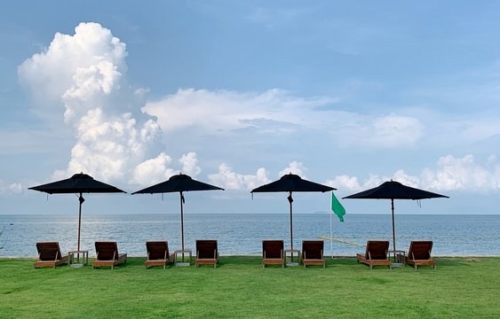Landscape of grass fields and background of blue sky white clouds with  umbrella and beach bed around private zone on the beach in hotel and resort, Holiday Vacation concept