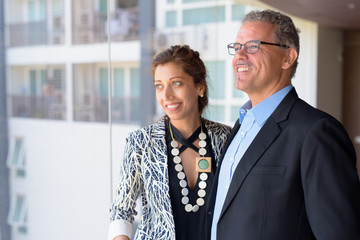 Happy Hispanic business couple together looking out the window of office building