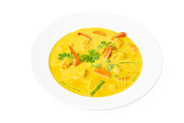 Closeup plate of thai yellow curry soup with coconut milk, shrimps, pineapple, carrot and green beans isolated at white background.