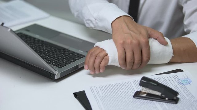 Businessman with broken arm in gypsum typing on laptop, trauma, workaholics