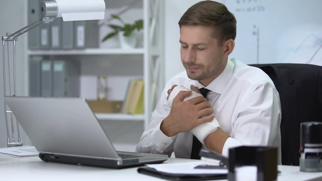 Workaholic man with broken arm in gypsum typing one hand on laptop pc, trauma